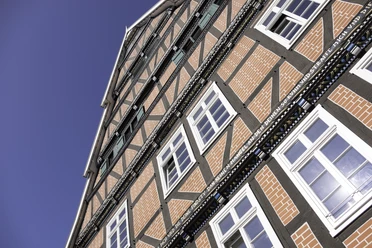 Haus Ottens Fachwerkhaus mit roten Ziegeln, weißen Sprossenfenstern und dekorativem Holzfachwerk vor blauem Himmel.