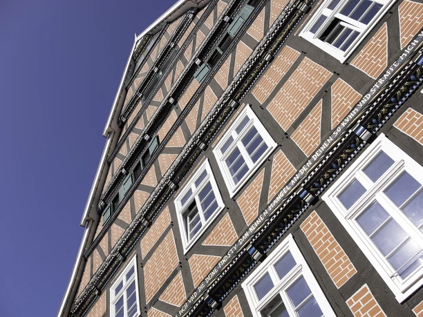 Haus Ottens Fachwerkhaus mit roten Ziegeln, weißen Sprossenfenstern und dekorativem Holzfachwerk vor blauem Himmel.