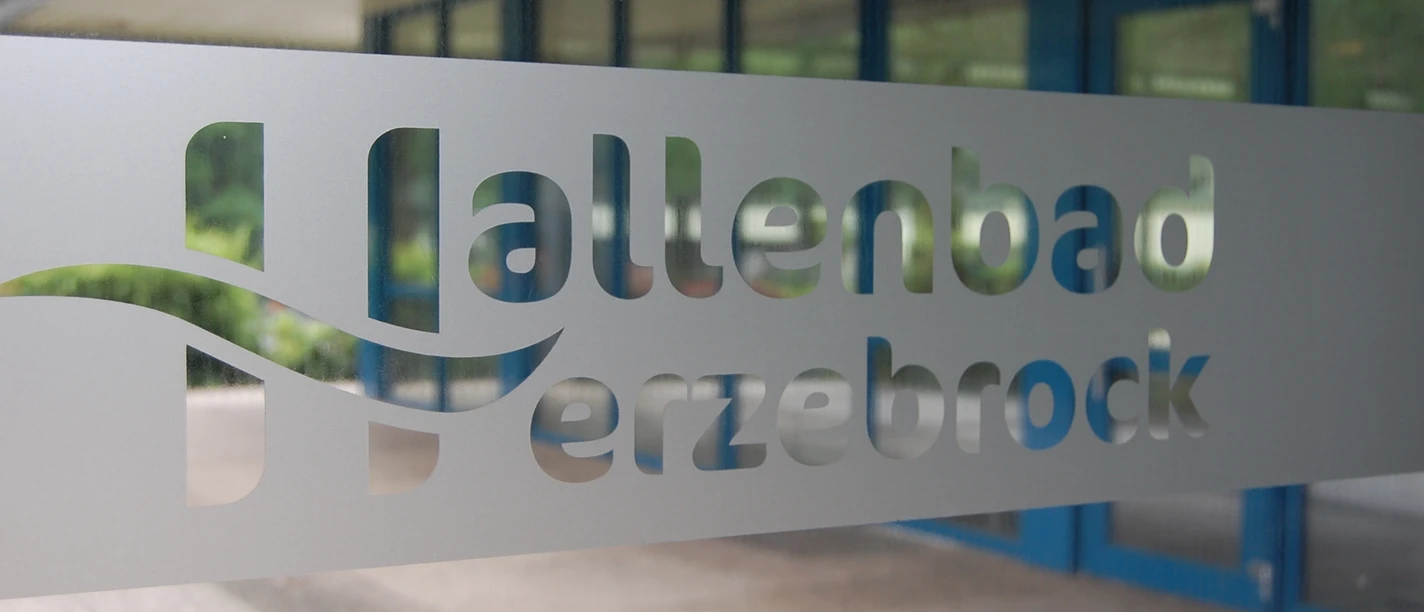 Hallenbad Herzebrock Schriftzug.JPG Eingangstür mit dem ausgeschriebenen Schriftzug "Hallenbad Herzebrock" aus mattiertem Glas.