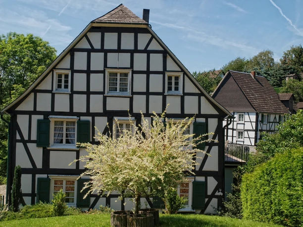 Eckenhagen Fachwerkhaus in ländlicher Umgebung mit grünem Garten und strahlend blauem Himmel im Hintergrund.