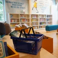 Ein heller Kinderbereich einer Bibliothek mit Bücherregalen, einem blauen Sofa und einem Korb voller Bücher.