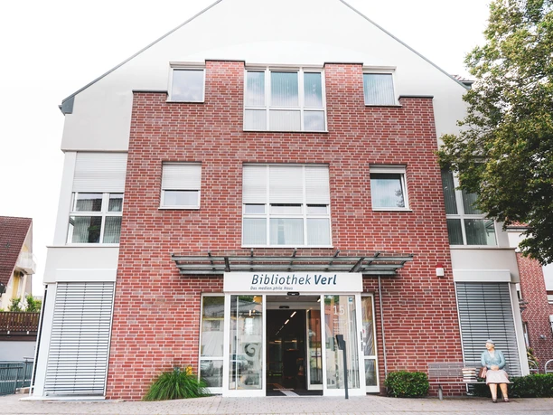 Eingang der Stadtbibliothek Verl, modernes Gebäude mit roter Ziegelfassade und großen Fenstern.