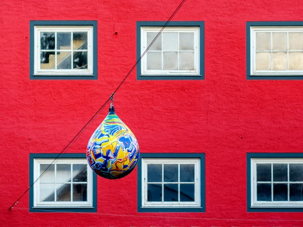 Kunst in der Innenstadt von Vlotho Im Vordergrund ein bemalter Fender, im Hintergrund eine Mauer von einem roten Haus mit Fenstern