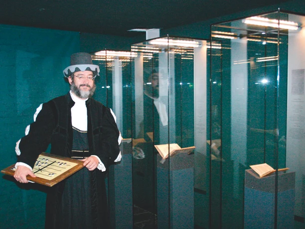 Annaberg-Buchholz_Adam Ries haus 2008_Matthias Förster.jpg Ein Mann in historischer Kleidung steht mit einem Rechenbrett in einem modernen Museum.