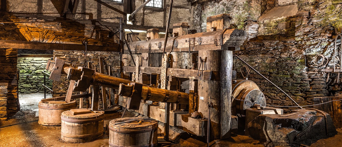 Interior view of a historic forge building with massive hammer mill and stone walls.