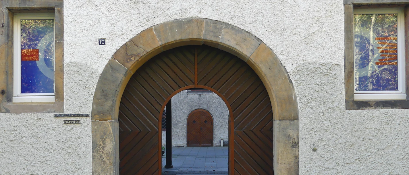 Rundbogen-Eingang aus Holz und Stein am Michaelskloster mit zwei bunten Fenstern links und rechts.