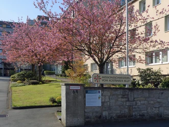 Missionshaus Neuenbeken mit blühendem Kirschbaum im Vordergrund und moderner Gebäudefassade.
