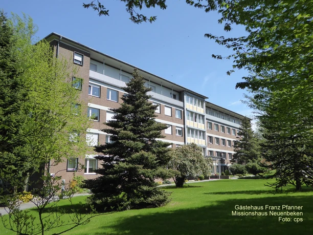 Missionshaus Neuenbeken Mehrstöckiges Backsteingebäude mit großen Fenstern, umgeben von grüner Vegetation und Nadelbäumen.