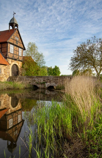 Gut Stockhausen Historisches Fachwerkgebäude an einem Wassergraben mit Steinbrücke, von Vegetation umgeben.