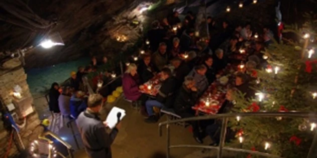 thumb_4301_Mettenschicht_im_Marie_Louise_Stolln.jpeg Menschen beim Feiern in einer beleuchteten, unterirdischen Höhle mit festlicher Dekoration.