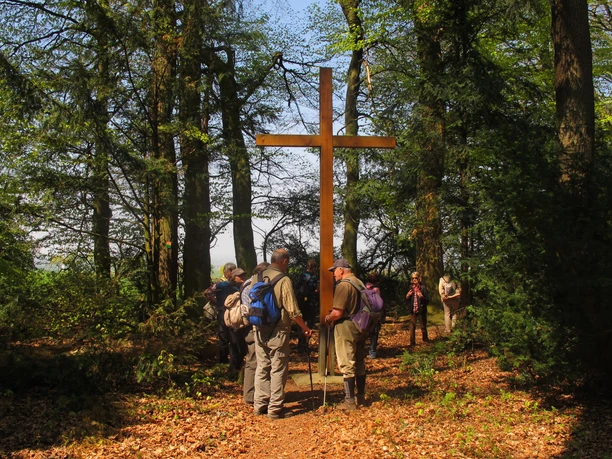 Holzkreuz umgeben von Wanderern, umgeben von Bäumen und Laub im Wald des Pestfriedhofs im Mittelholz.