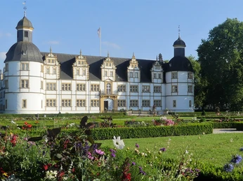 Historisches Schloss Neuhaus in Paderborn umgeben von gepflegtem Park, blühenden Blumenbeeten und Bäumen.