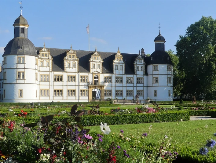 Historisches Schloss Neuhaus in Paderborn umgeben von gepflegtem Park, blühenden Blumenbeeten und Bäumen.