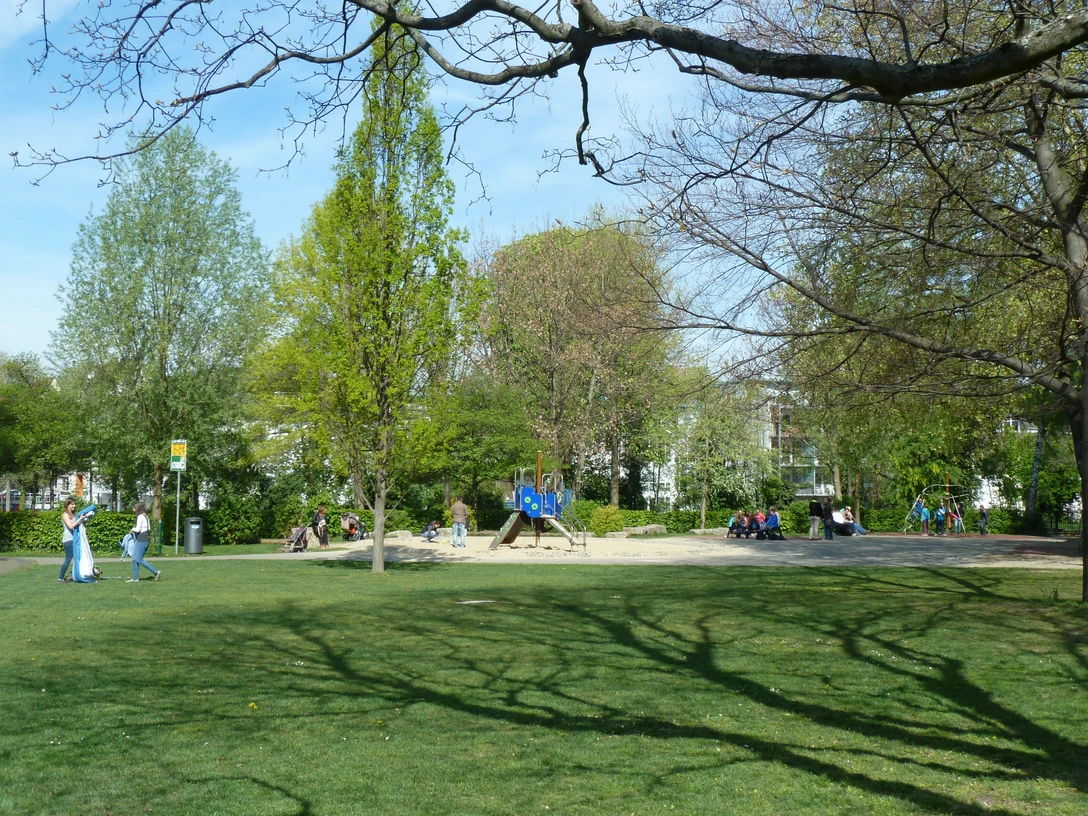 Spielplatz im Paderquellgebiet Grüner Spielplatz mit Klettergerüst und Sitzbereich zwischen Bäumen, Menschen genießen einen sonnigen Tag.