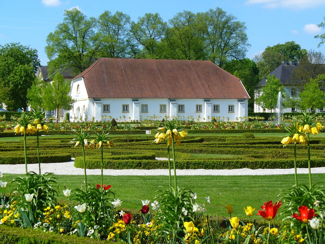 Historisches Gebäude hinter symmetrischen Gartenanlagen mit bunten Blumen und gepflegten Wegen.