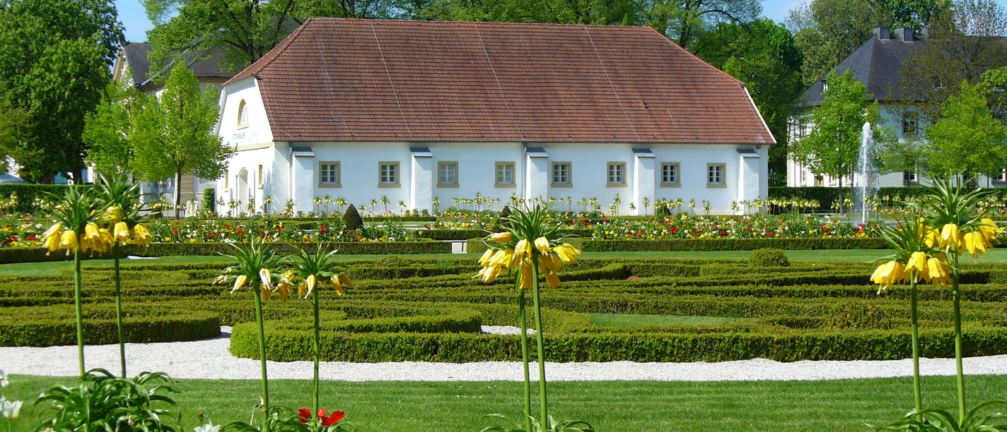 Städtische Galerie in der Reithalle Historisches Gebäude hinter symmetrischen Gartenanlagen mit bunten Blumen und gepflegten Wegen.