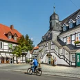 Historische Fachwerkhäuser mit markantem Türmchen und Radfahrer bei sonnigem Wetter in Bad Essen.