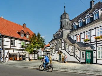 Historische Fachwerkhäuser mit markantem Türmchen und Radfahrer bei sonnigem Wetter in Bad Essen.