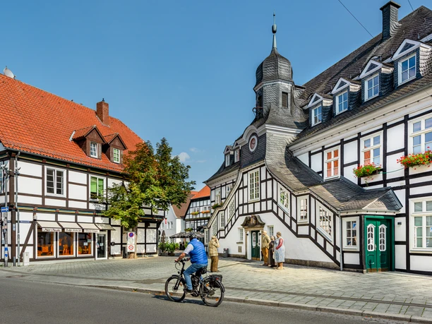 Historische Fachwerkhäuser mit markantem Türmchen und Radfahrer bei sonnigem Wetter in Bad Essen.