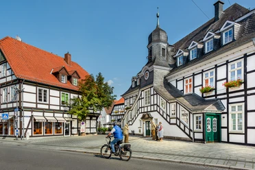 Rietberg-RathausRadfahrer-prowiGT-Wallenfang.jpg Historische Fachwerkhäuser mit markantem Türmchen und Radfahrer bei sonnigem Wetter in Bad Essen.