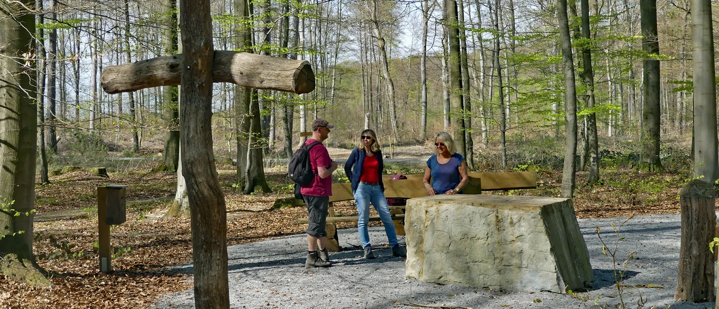 Friedwald Nonnenbusch Drei Menschen stehen an einem Steintisch im Wald, umgeben von Bäumen und einem Holzkreuz.