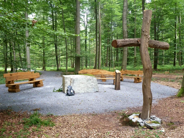 Andachtsplatz im Friedwald Nonnebusch mit Holzbänken, einem großen Kreuz und umgeben von Bäumen.