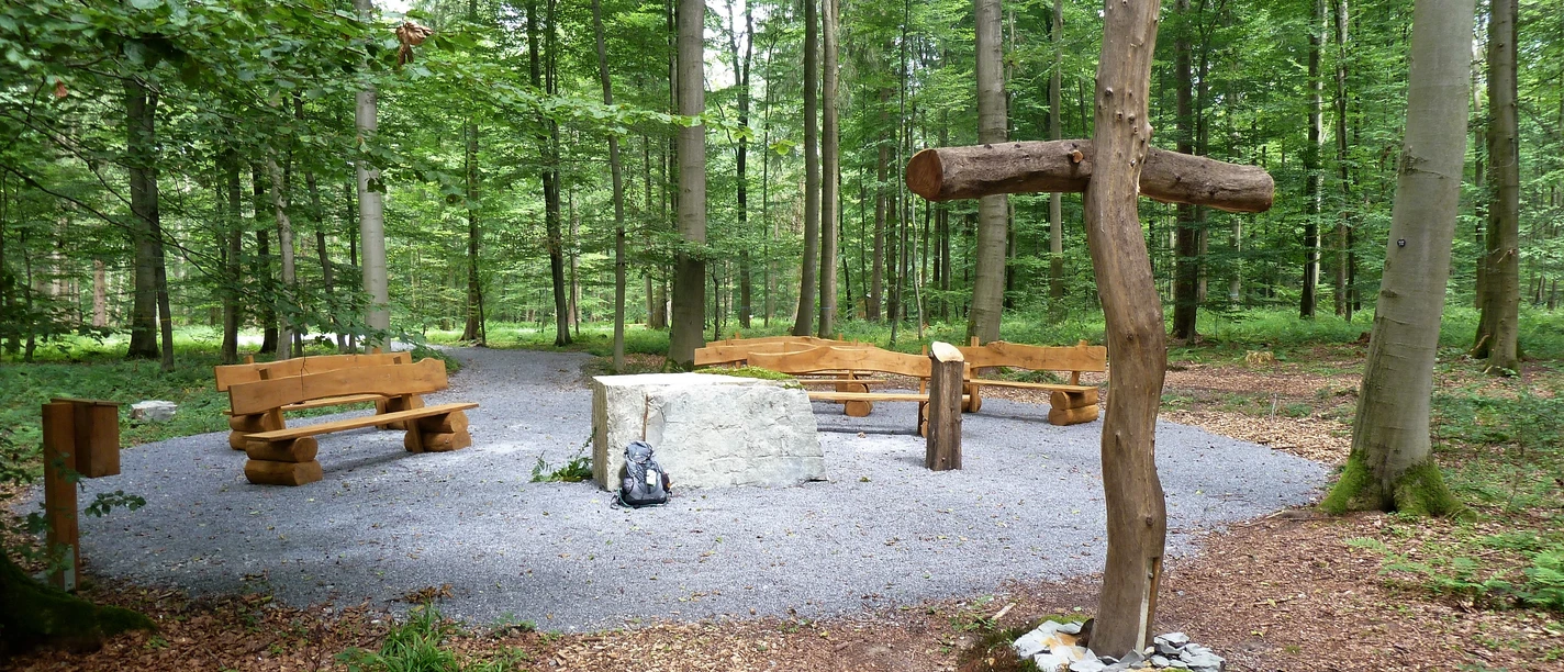 Friedwald Nonnebusch, Andachtsplatz Andachtsplatz im Friedwald Nonnebusch mit Holzbänken, einem großen Kreuz und umgeben von Bäumen.