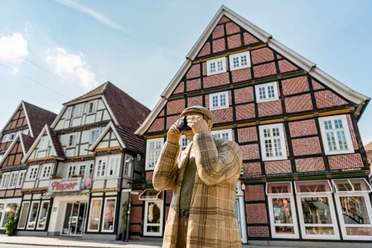 Rietberg Innenstadt - Alltagsmensch Eine Holzfigur in traditioneller Kleidung fotografiert Fachwerkhäuser in einer historischen deutschen Stadt.