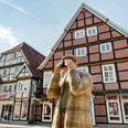 Rietberg Innenstadt - Alltagsmensch Eine Holzfigur in traditioneller Kleidung fotografiert Fachwerkhäuser in einer historischen deutschen Stadt.