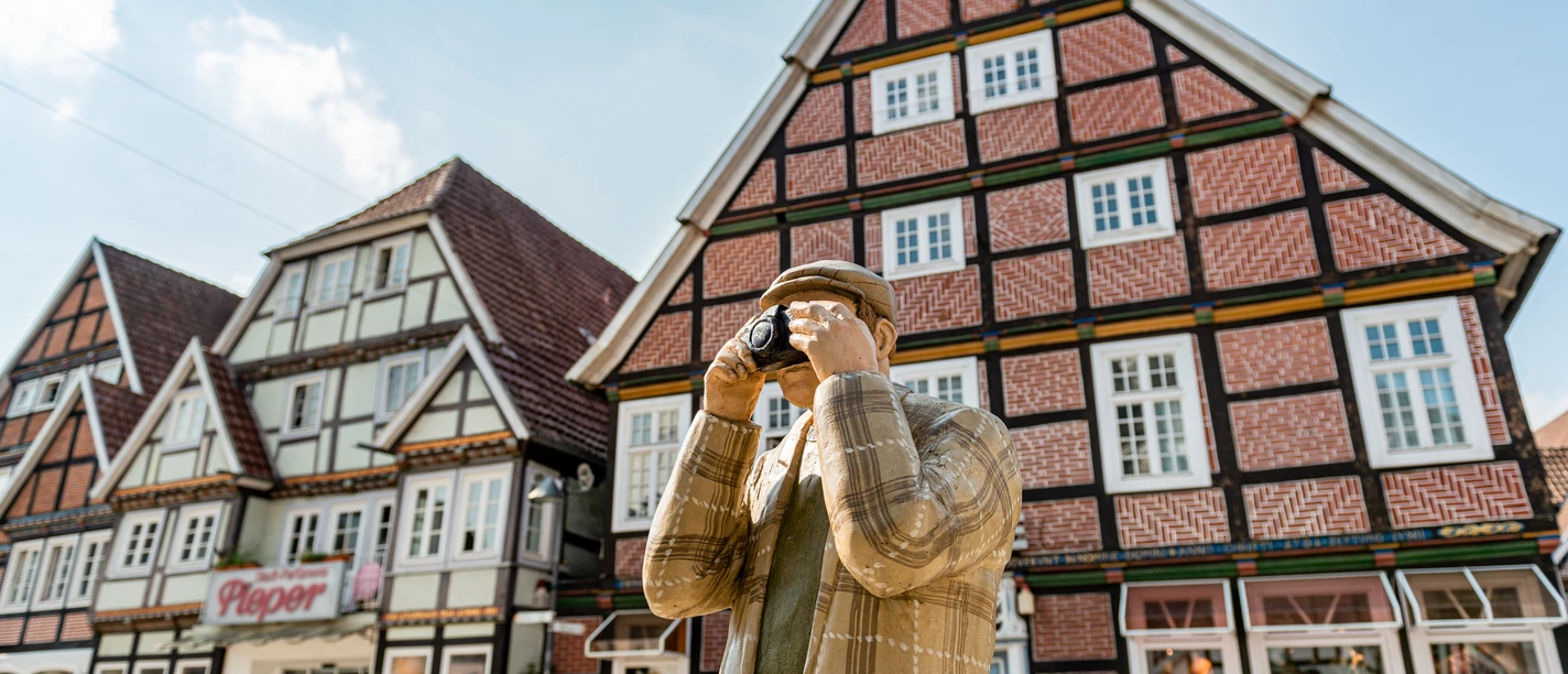 Rietberg Innenstadt - Alltagsmensch Eine Holzfigur in traditioneller Kleidung fotografiert Fachwerkhäuser in einer historischen deutschen Stadt.