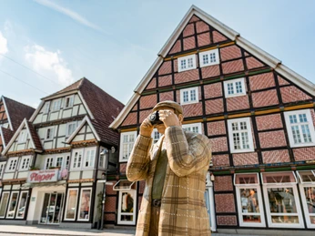 Rietberg Innenstadt - Alltagsmensch Eine Holzfigur in traditioneller Kleidung fotografiert Fachwerkhäuser in einer historischen deutschen Stadt.