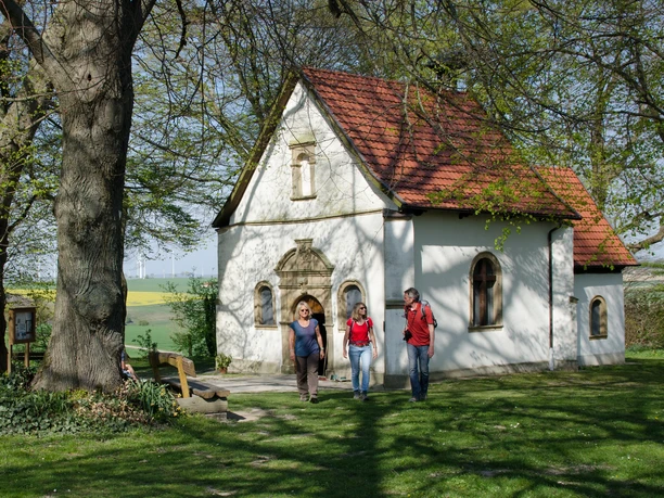 Kapelle "Zur Hilligen Seele" Eine kleine Kapelle mit rotem Ziegeldach steht in einer grünen, von Bäumen umgebenen Landschaft.