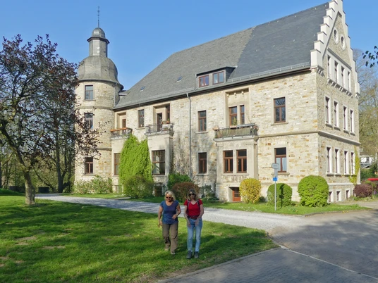 Schloß Hamborn Eine Gruppe von Menschen spaziert vor einer historischen Schlossgebäude mit Turm und Gartenanlage.