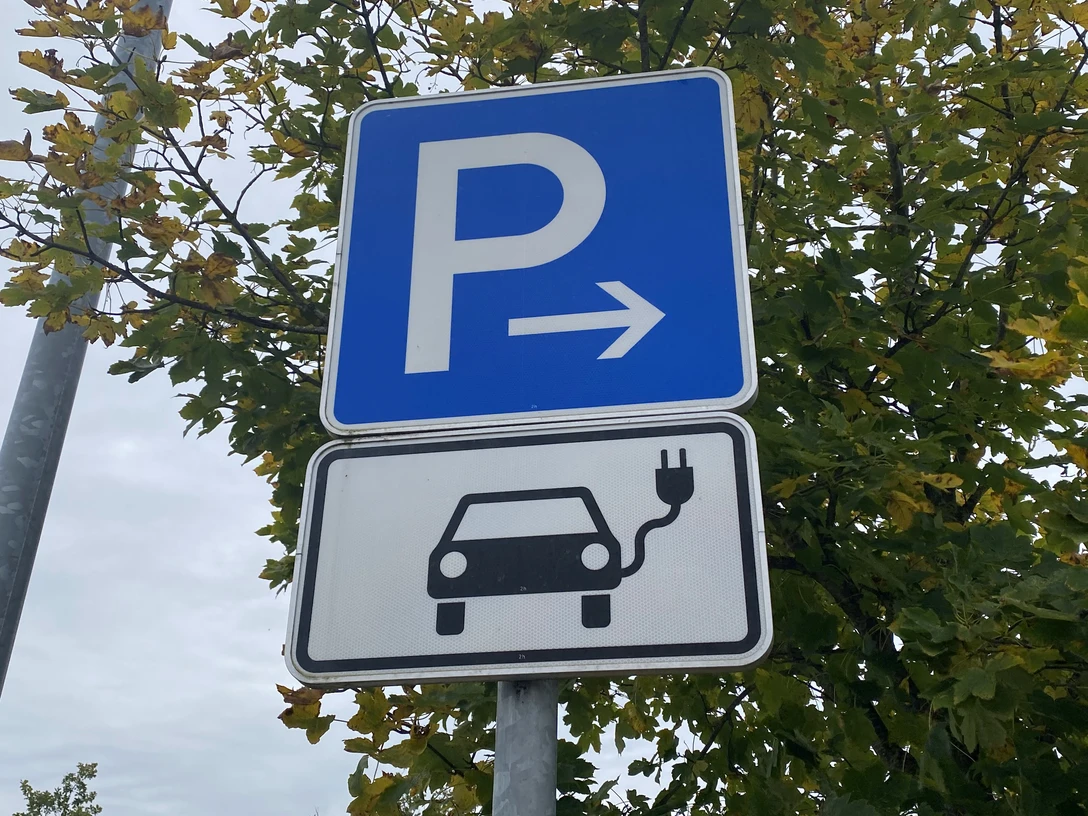 Symbolbild: E-Tankstelle Parkschild mit Elektroauto-Symbol in herbstlicher Umgebung, deutet auf Ladestation für E-Autos hin.