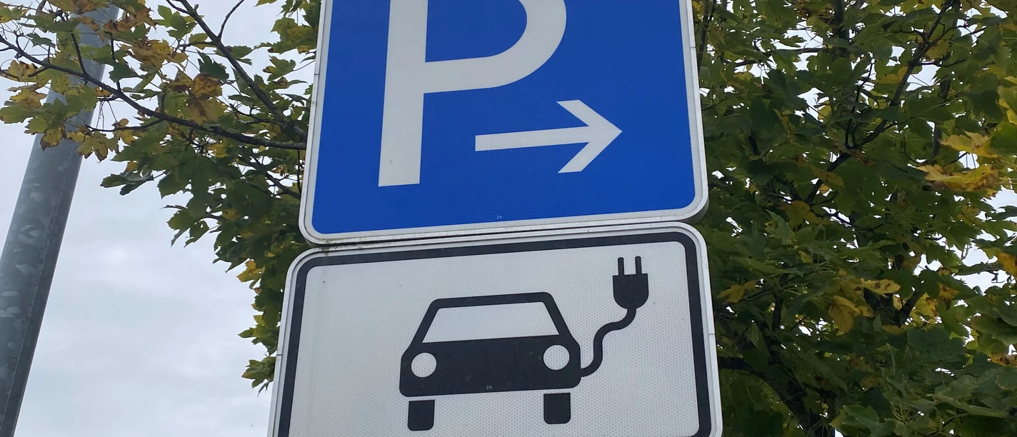 Symbolbild: E-Tankstelle Parkschild mit Elektroauto-Symbol in herbstlicher Umgebung, deutet auf Ladestation für E-Autos hin.