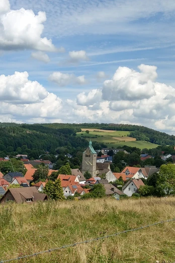 Neuenbeken mit seiner zentralen Kirche im Vordergrund, umgeben von Wiesen und bewaldeten Hügeln.