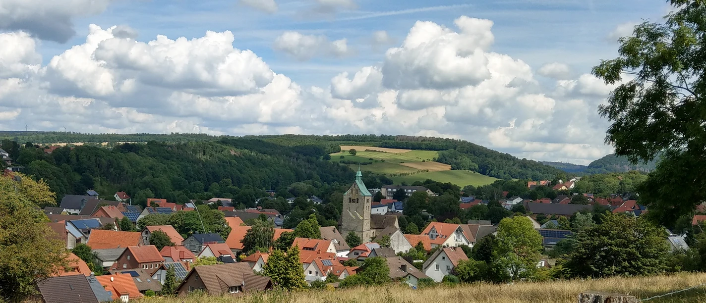 Blick auf Neuenbeken Neuenbeken mit seiner zentralen Kirche im Vordergrund, umgeben von Wiesen und bewaldeten Hügeln.