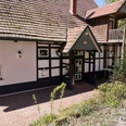 Café Waldkristall.jpg Fachwerkhaus mit grün-weißen Details, rotem Ziegeldach und Außenbereich, umgeben von Bäumen und Pflanzen.