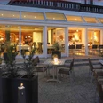 Deekes-Quellenhof_Luebbecke.JPG Restaurant-Bereich eines Gebäudes mit Außenterrasse, abends beleuchtet, mit Kerzen auf Tischen.