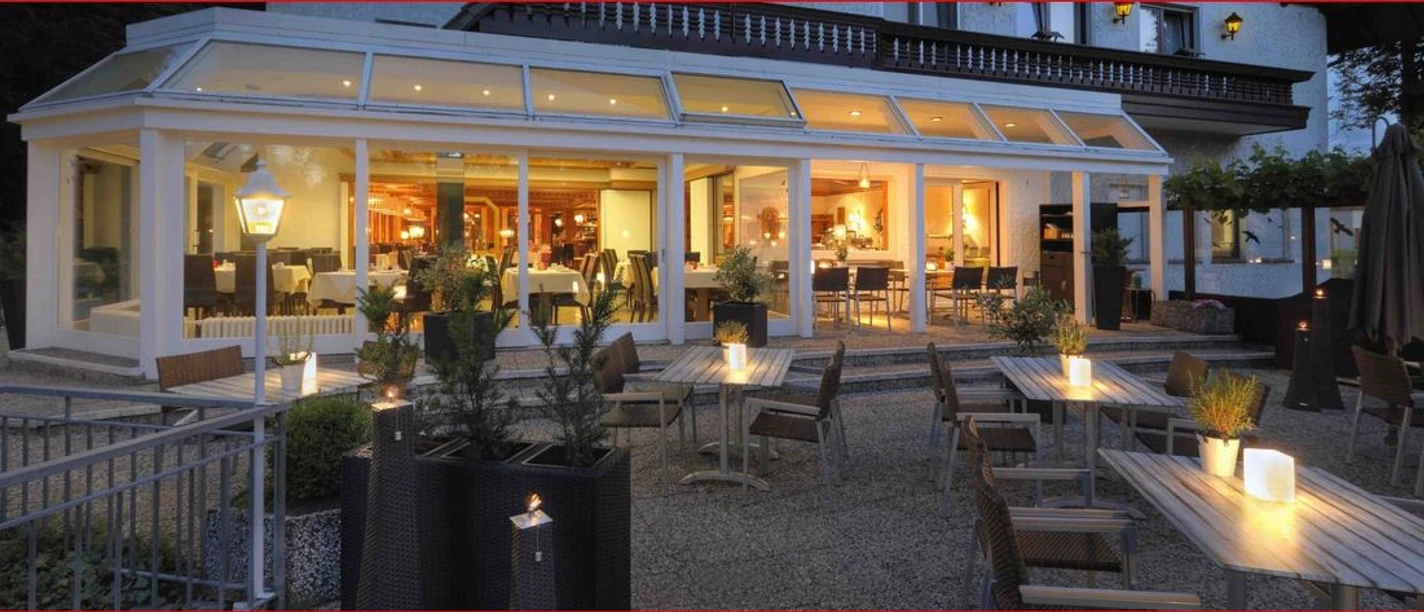 Deekes-Quellenhof_Luebbecke.JPG Restaurant-Bereich eines Gebäudes mit Außenterrasse, abends beleuchtet, mit Kerzen auf Tischen.
