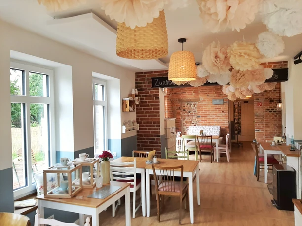 Kaffeeküche in Hille Helle Kaffeeküche mit Holzfußboden, gemusterten Hängelampen, dekorativen Blumen und Holzstühlen.