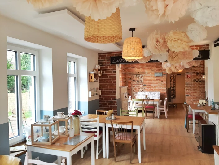 Kaffeeküche in Hille Helle Kaffeeküche mit Holzfußboden, gemusterten Hängelampen, dekorativen Blumen und Holzstühlen.