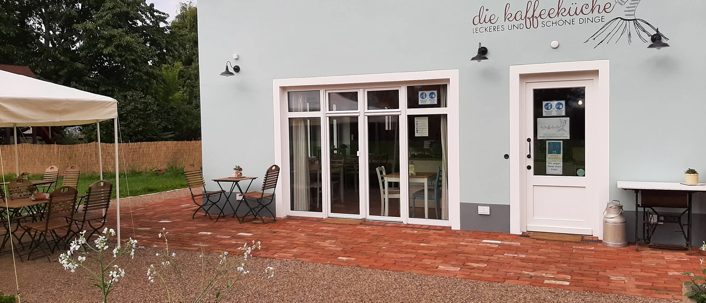 Kaffeeküche in Hille Kaffeeküche mit Terrasse, weißen Wänden und Holzelementen, umgeben von Natur, bietet Freiluftplätze.