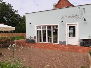 Kaffeeküche in Hille Kaffeeküche mit Terrasse, weißen Wänden und Holzelementen, umgeben von Natur, bietet Freiluftplätze.