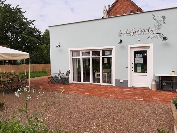 Kaffeeküche in Hille Kaffeeküche mit Terrasse, weißen Wänden und Holzelementen, umgeben von Natur, bietet Freiluftplätze.