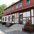 Fachwerkgebäude mit roten Akzenten, Treppenstufen führen zum Eingang, von Bänken flankiert.