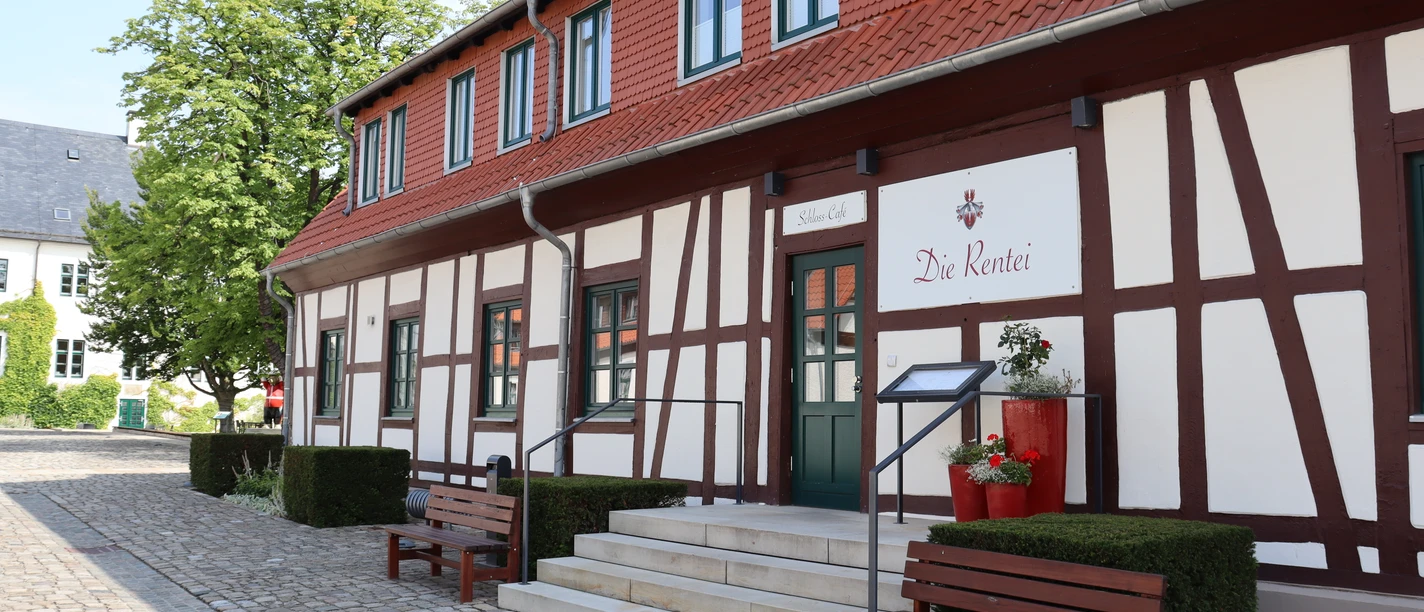 Fachwerkgebäude mit roten Akzenten, Treppenstufen führen zum Eingang, von Bänken flankiert.