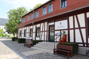 Die Rentei Fachwerkgebäude mit roten Akzenten, Treppenstufen führen zum Eingang, von Bänken flankiert.