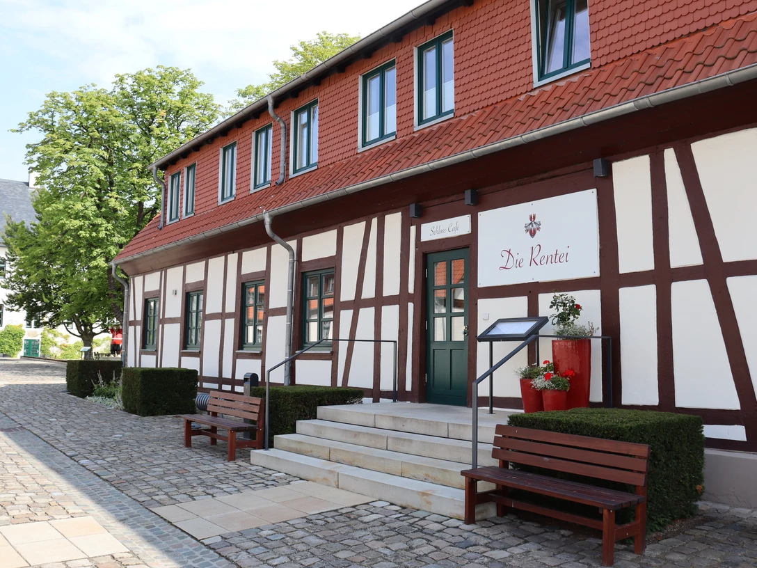 Die Rentei Fachwerkgebäude mit roten Akzenten, Treppenstufen führen zum Eingang, von Bänken flankiert.