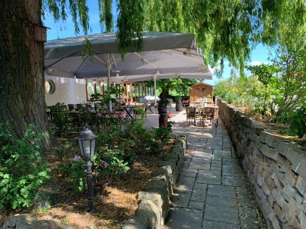 Dreimädelhaus Außenbereich eines Restaurants mit überdachten Sitzgelegenheiten, umgeben von grüner Natur und Backsteinmauer.